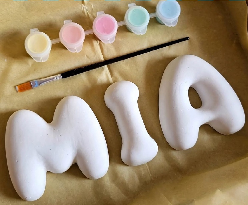 Kit con las letras MIA, cinco potes de pintura pastel y un pincel sobre papel de seda